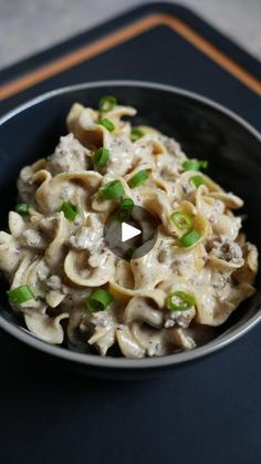 a black bowl filled with pasta and green onions on top of a blue place mat