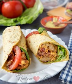 two burritos on a plate with lettuce and tomatoes in the background