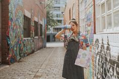 a woman standing next to a wall with graffiti on it and holding a water bottle