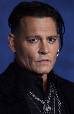 a close up of a person wearing a black shirt and silver necklaces on his neck