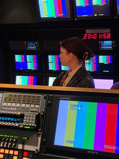 a woman sitting at a desk in front of several televisions with color bars on them