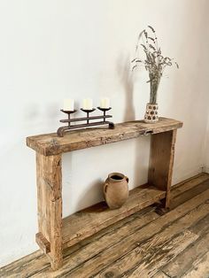 an old wooden table with candles on it and a vase sitting next to the shelf