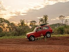 a red car parked on the side of a dirt road in front of some trees