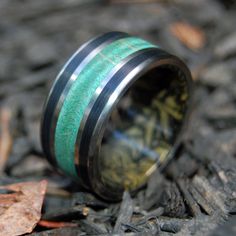 a green and black wedding ring with wood inlays on the inside, sitting on top of leaves