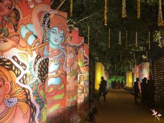 people are walking down a path lined with colorfully painted walls and lights at night