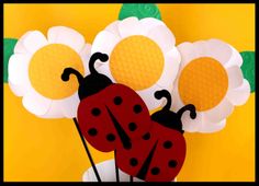 paper flowers and ladybugs in a vase with daisies on the side, against a yellow background