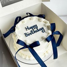 a white birthday cake with blue ribbon in a box