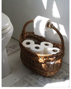 two rolls of toilet paper in a wicker basket next to a toilet with the lid up