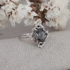 a close up of a ring on top of a white surface with flowers in the background