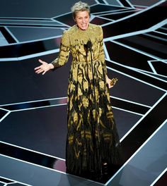 an older woman in a black and gold dress on stage with her hands out to the side