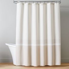 a white shower curtain in a bathroom next to a bathtub and wooden flooring