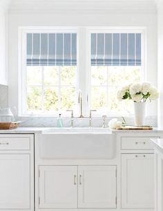 a kitchen with white cabinets and blue roman shades on the windowsills above the sink