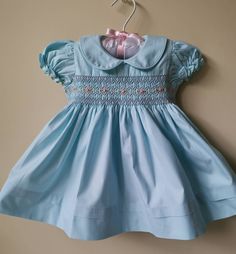 This beautiful dress is hand smocked with matching blue and hand embroidered with soft pink roses and green leaves on the bodice.  Dress is fully lined with soft cotton material. The back closes with a zip and tie sashes.  100% Cotton  Cold gentle machine wash Size 3-6 months (AU 00) Length 14.5" Chest circumference 19.5" Size 6-12 months (AU 0) Length 16" Chest circumference 20" Size 1 Length 18" Chest circumference 21" Size 2 Length 20" Chest circumference 22" Size 3 years  Length 22"  Chest c Blue Embroidered Cotton Smocked Dress, Fitted Light Blue Smocked Dress With Smocked Cuffs, Light Blue Fitted Smocked Dress With Smocked Cuffs, Cute Blue Dresses With Smocked Cuffs, Cute Blue Dress With Smocked Cuffs, Cute Fitted Dress With Smocked Cuffs, Light Blue Smocked Dress With Ruffles And Fitted Style, Cute Blue Dress With Smocked Back, Cute Light Blue Dress With Smocked Back