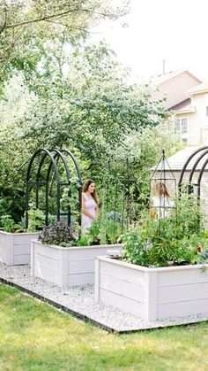 a woman is standing in the middle of a garden with several raised planter boxes