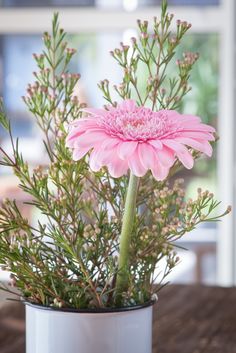 a pink flower in a white vase on a table