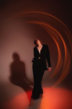 a woman standing in front of a white wall wearing a black suit and red shoes