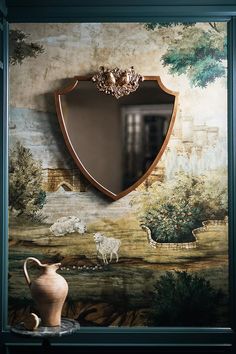 a vase sitting next to a mirror in front of a wall with sheep painted on it