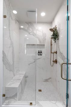 a bathroom with white marble walls and flooring, shower head, and glass door