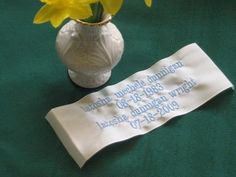 a white vase with yellow flowers in it on a green table cloth next to a napkin