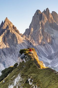 a man standing on top of a mountain next to a lush green hillside covered in grass