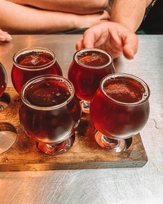 four glasses of wine sitting on top of a wooden tray next to another glass filled with liquid