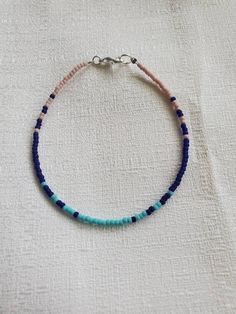 a blue and pink beaded bracelet on a white cloth with a silver hook clasp