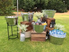 several metal buckets filled with bottles and water on top of grass next to trees