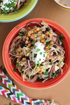 a bowl filled with coleslaw and corn on top of a table next to two colorful paper straws