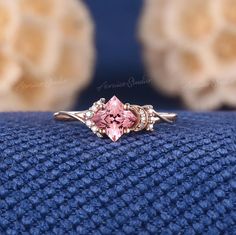 a close up of a ring with a pink stone on the front and side, sitting on a blue cloth