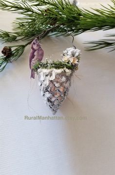 a pine cone ornament hanging from a tree branch with flowers and birds on it