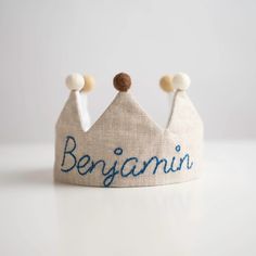 a white crown with blue writing on it and two small balls at the top that say benjamin