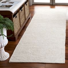 a white rug on the floor in front of a window with a basket and plant