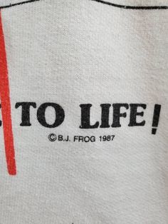 "Here is a vintage sweatshirt with some truth to tell. Reads: There's More To Life! There is a pinpoint hole in the right armpit, as pictured. Size is equivalent to men's medium. Size 38. Tag reads: BJ Frogs. Measurements (taken lying flat): Shoulder (seam to seam) - 15\" Chest (armpit to armpit) - 21 1/4\" Sleeve length (shoulder seam to cuff) - 20 1/4\" Overall length - 23 3/4\" Present day, there is no more intimate way to time travel than to wear a vintage piece of clothing. Like you, the fa Vintage Cotton Sweatshirt With Slogan, Vintage Crew Neck Shirt With Cartoon Print, Vintage Fruit Print Crew Neck Tops, Dinosaur Shirt Vintage, Vintage Long Sleeve T-shirt With Funny Print, Vintage Crew Neck T-shirt With Cartoon Print, 1980s Kids, Band Hoodies, Tool Band