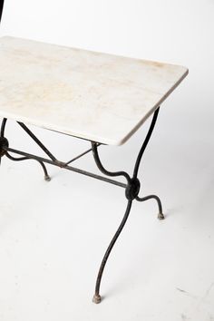 a white marble top table with wrought iron legs on an isolated white surface, against a plain background