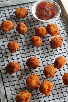 some fried food is sitting on a cooling rack next to a bowl of ketchup