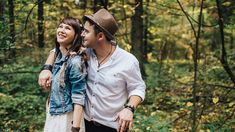 a man and woman standing next to each other in the woods