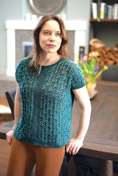 a woman standing in front of a table wearing brown pants and a teal sweater