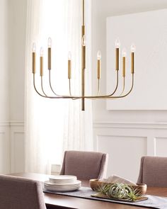 a chandelier hanging over a dining room table with plates and bowls on it