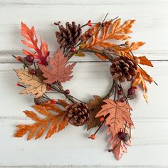 a wreath made out of leaves and acorns on a white wooden surface with pine cones