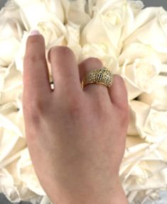 a person's hand holding a wedding ring in front of a bouquet of white roses