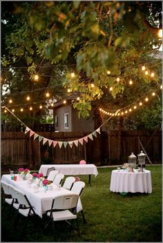 an image of a backyard party with lights strung from the trees and tables covered in white tablecloths