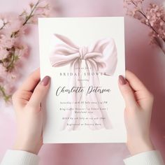 a person holding up a card with a pink bow on it and flowers in the background