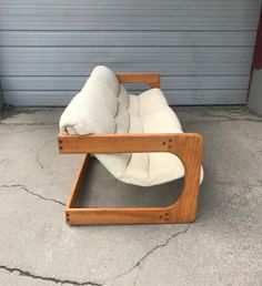 a wooden chair sitting on top of cement next to a garage door with a white pillow