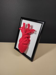 a red heart in a black frame on a table