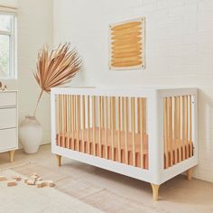 a baby crib in a white room next to a dresser and window with palm leaves on it