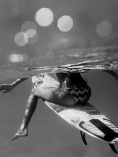 a woman sitting on top of a surfboard under the water's surface in black and white