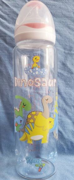 a baby bottle with dinosaurs on it sitting on a blue cloth covered bedding area