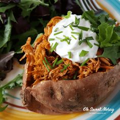 a close up of a baked potato on a plate with greens and sour cream in the center