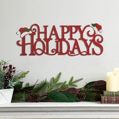 a holiday sign on a mantle with candles and evergreens in the foreground that reads happy holidays