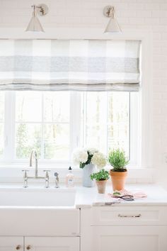 a kitchen with white cabinets and counter tops next to a window filled with potted plants